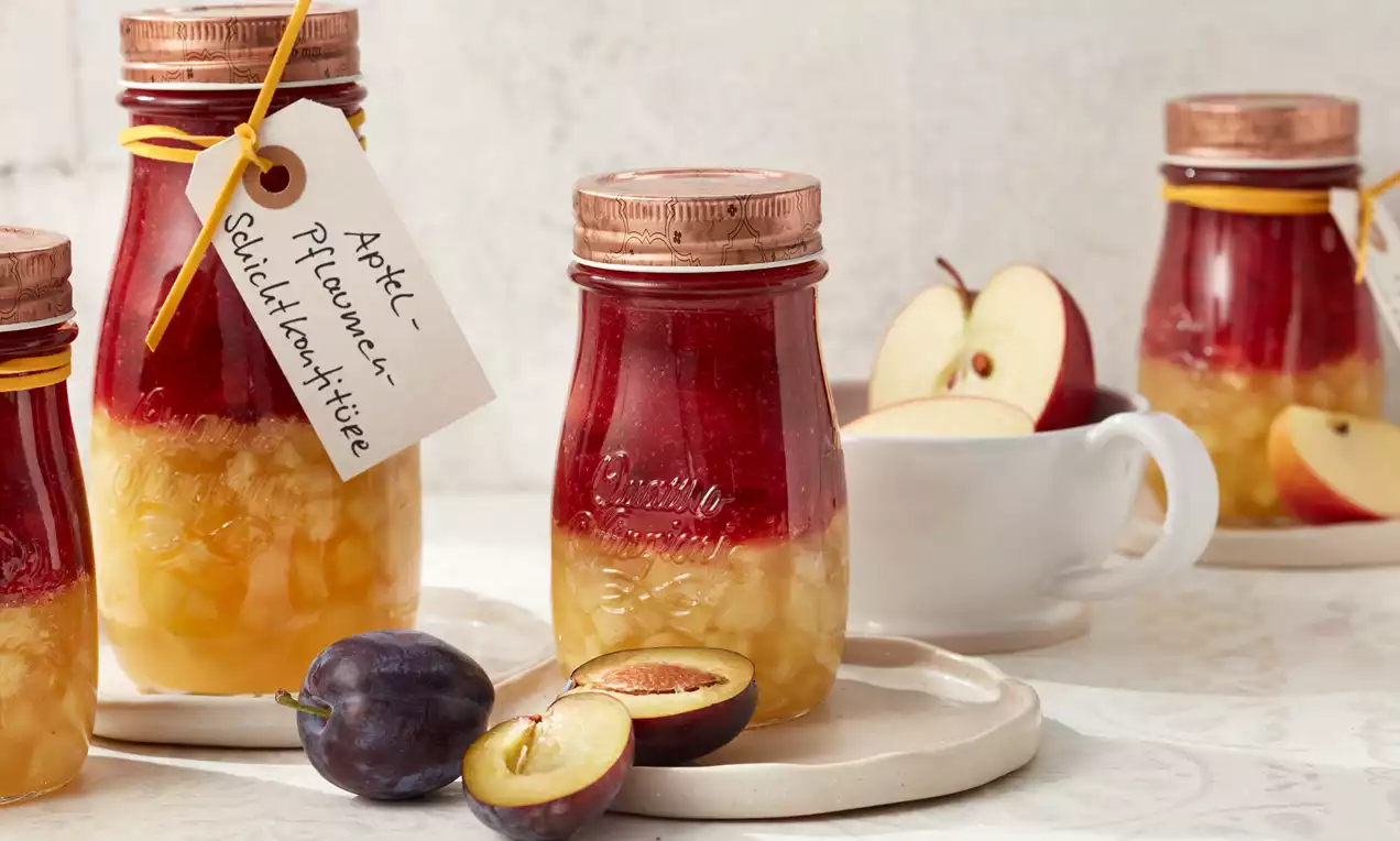 Apfel-Pflaumen-Schichtkonfitüre in Gläsern mit bronzefarbenen Deckeln, gelber Obstschicht, satter roter Fruchtschicht und beigefarbenem Anhänger